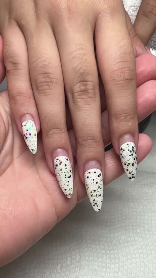 Long almond Gel-X nails in milky white with black speckle nail art